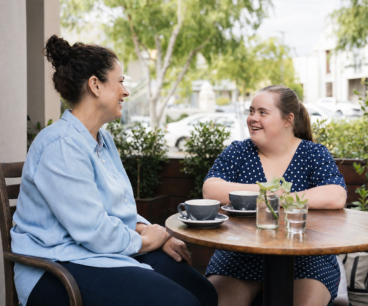 Divine Path Care support worker having a relaxed conversation with an NDIS participant at an outdoor café